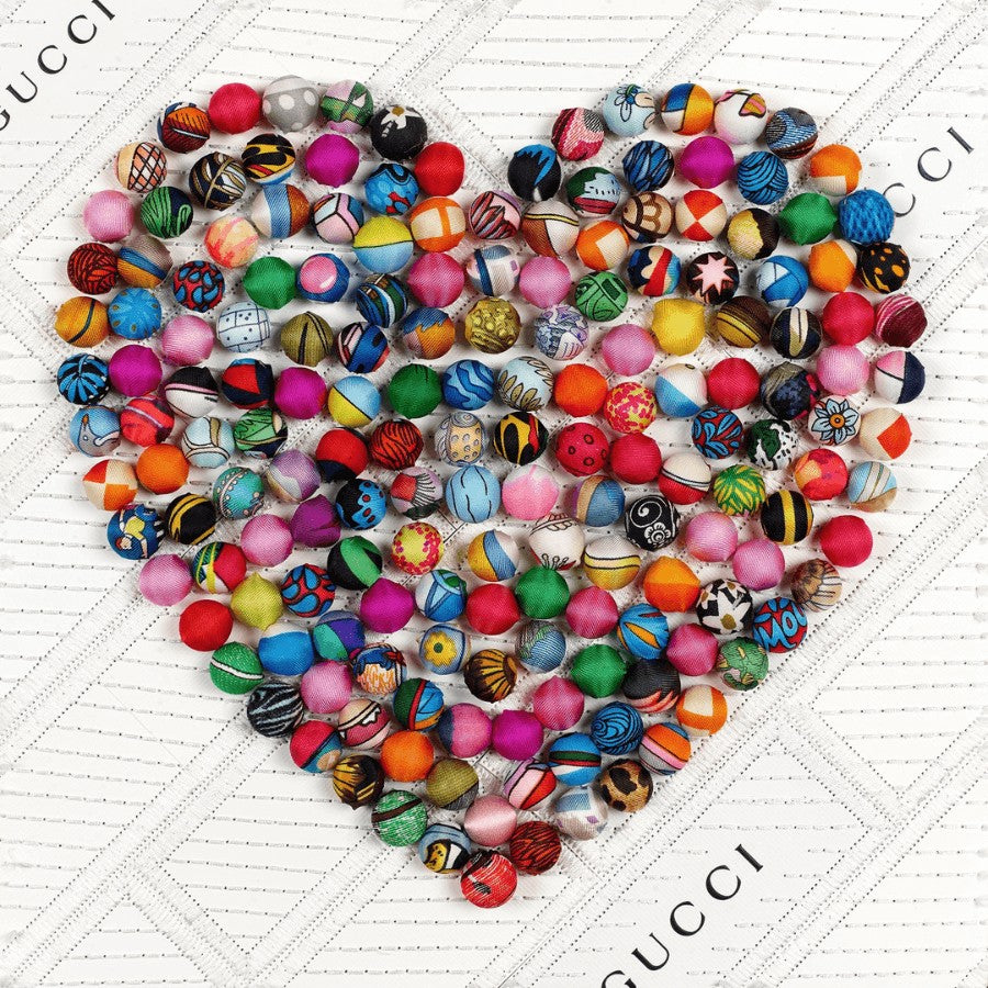 The Pom-pom Heart begins by deconstructing and reconstructing luxury boxes and bags to form the background for the piece. The heart shape is created by hand rolling pom-poms and mounting them through the background. Each pom-pom is created with up-cycled luxury scarves that are hand selected for their patterns. When all the elements are combined, they make for a rich and bold visual experience. 12" x 12" x 2" in size. The art comes framed in acrylic and is signed and numbered by the artist.  Items may vary.