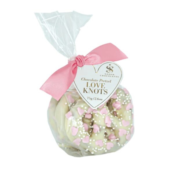 These crunchy pretzels are full of love! Enjoy three large pretzel knots coated in a thick layer of white chocolate and sprinkled with pink mini sugar hearts, and white mini pearls.  Each set of pretzels is placed in a clear bag with a pink satin ribbon and branded tag.  63g / 2.2oz. 12 per case. Shelf life - 12 months.