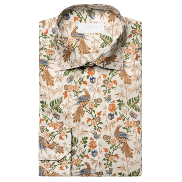 A sophisticated dress shirt made from a breathable and shiny 100% cotton fine twill material, woven with a mélange yarn. This standout item showcases a repeated pattern of a finely intricate peacock in classic hues, inspired by the historical designs of renowned Italian stationer Rossi 1931. The inclusion of mother-of-pearl buttons and meticulous 2mm stitching on the collar and cuffs elevates the elegance of the overall attire. 100% Cotton. Mother Of Pearl Buttons. Wrinkle Free.